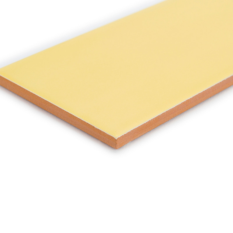 Un carreau rectangulaire jaune pâle repose sur une surface blanche, présentant une couche supérieure lisse avec un bord brun ora