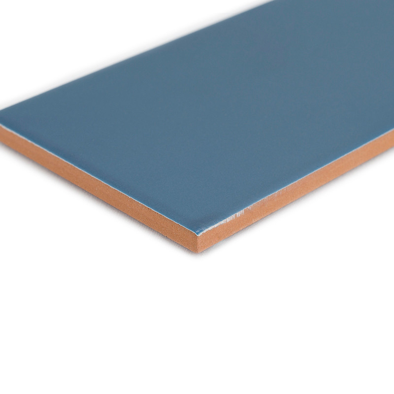 Un carreau de céramique rectangulaire bleu repose à plat sur un fond blanc, montrant sa surface lisse et son bord marron contras