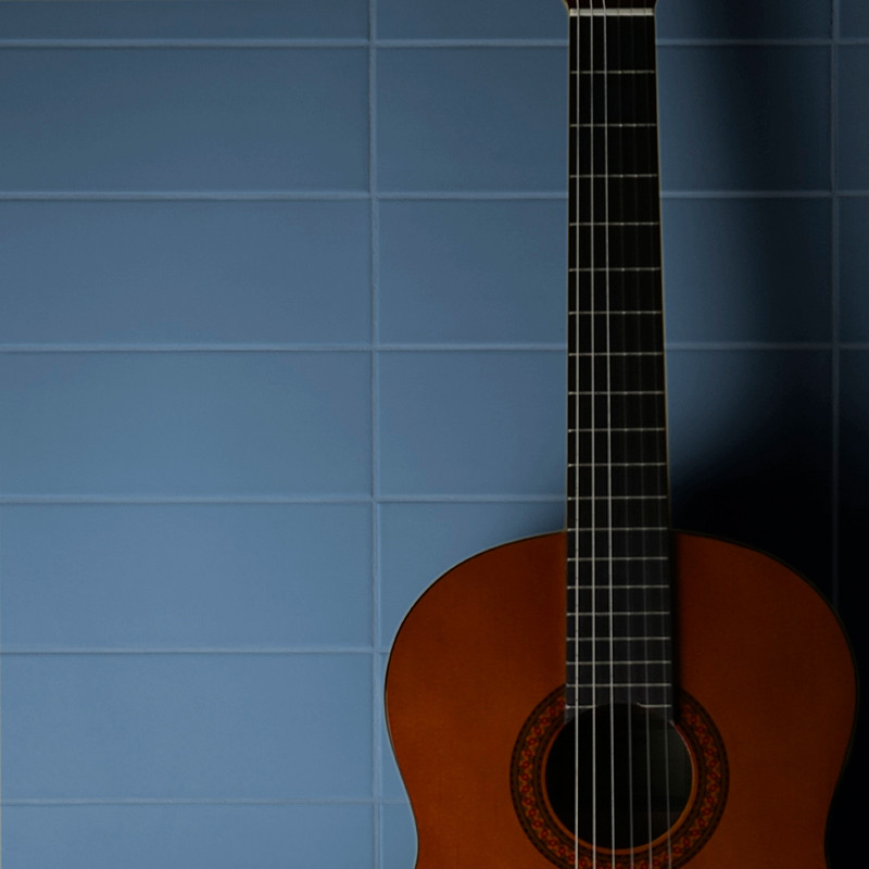 Une guitare classique se dresse sur un fond de carreaux carrés bleus, projetant une douce ombre sur le mur.