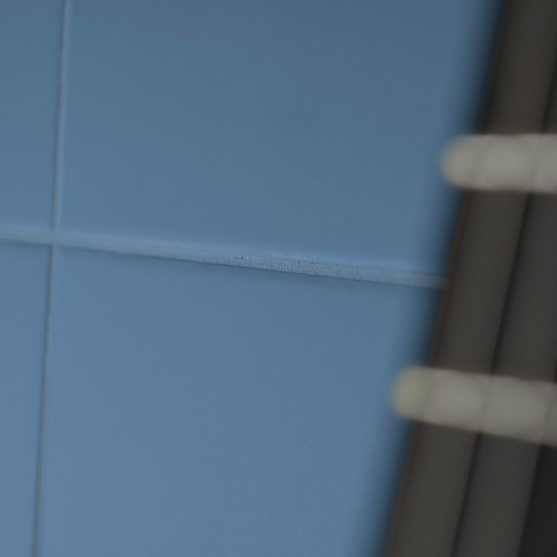 Les carreaux de céramique bleue forment un motif en grille sur un mur, avec un tuyau métallique partiellement visible sur le côt