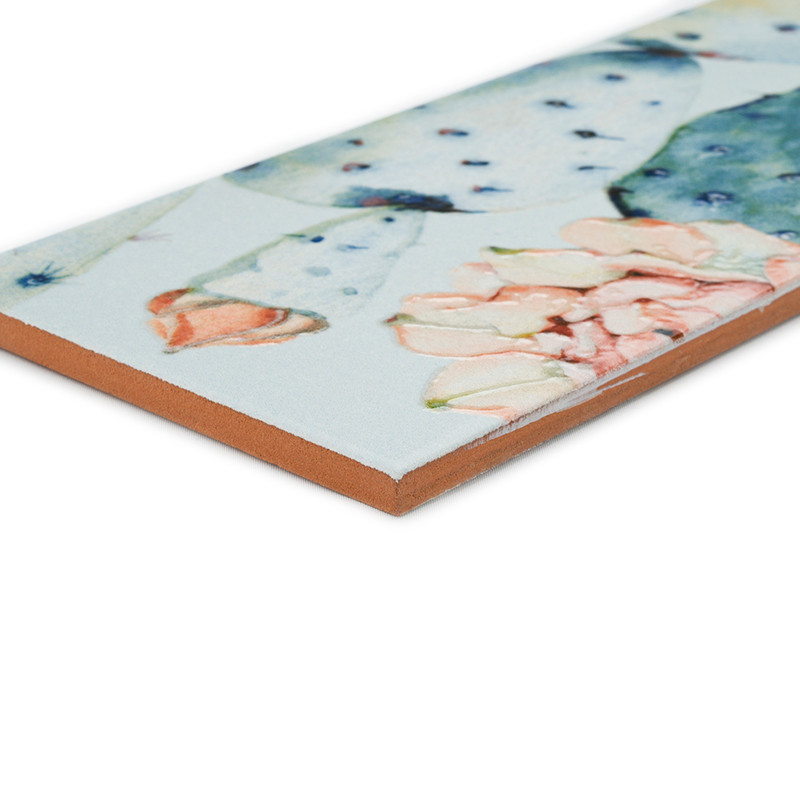 A rectangular ceramic tile displays watercolor-style cactus illustrations with soft green and pink hues, viewed from a low angle