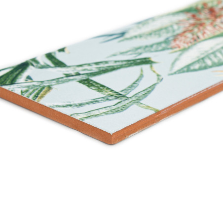 Eine Keramikfliese zeigt ein detailliertes tropisches Blattmuster in Grün und Orange vor einem weißen Hintergrund.