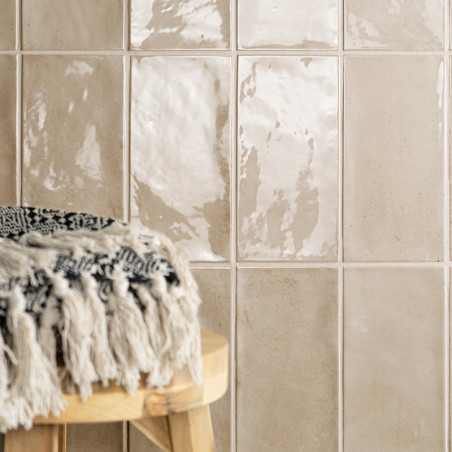 Glanzende beige tegels reflecteren het licht, waardoor een glanzend oppervlak ontstaat. Een ronde houten kruk met zwart-wit text