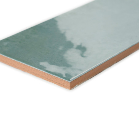 Eine rechteckige Keramikfliese mit einer glänzenden blaugrünen Oberfläche und einem wolkigen Muster liegt auf einem glatten brau