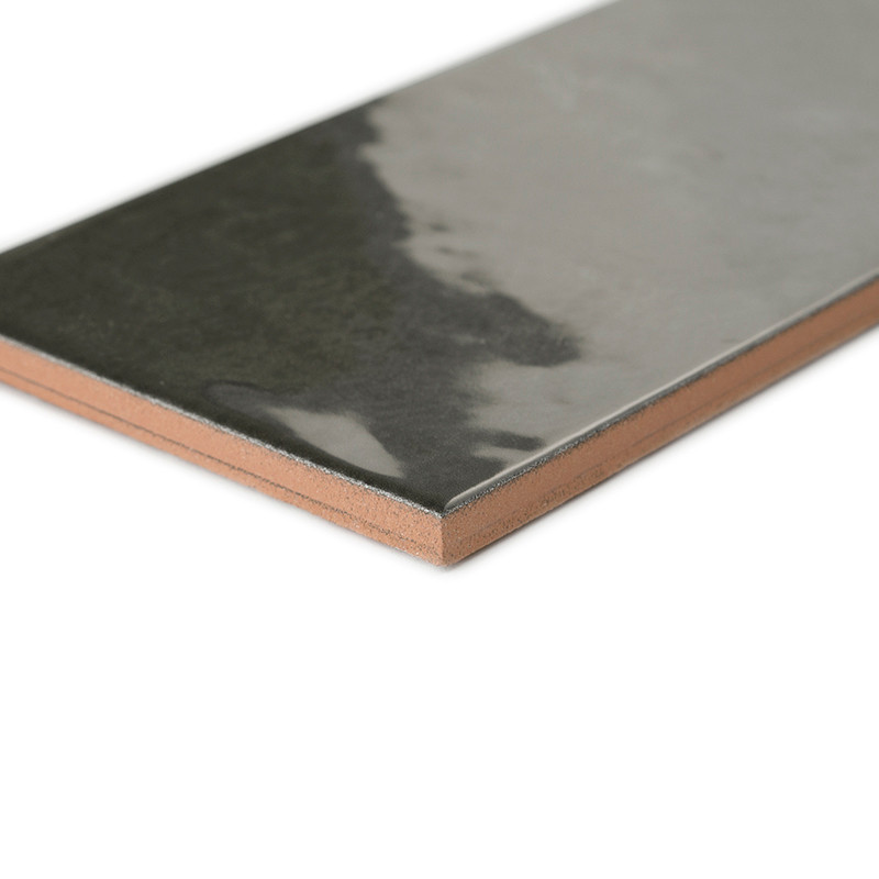 A rectangular, glossy ceramic tile lies diagonally, reflecting light on its dark surface. The tile is set against a plain white 