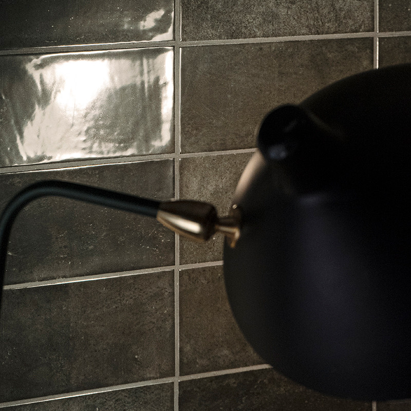 A matte black lamp extends over a glossy, reflective tile wall, creating a contrast between light and dark textures.