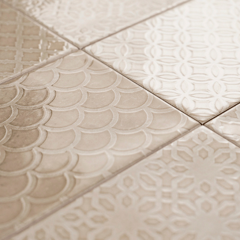 Les carreaux de céramique présentent des motifs texturés variés et des finitions brillantes, disposés en grille, créant une surf