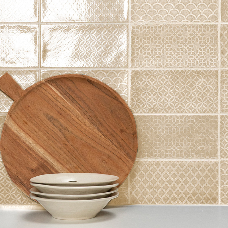 A wooden cutting board leans against a textured, beige-patterned tile wall, with three stacked white bowls in the foreground.