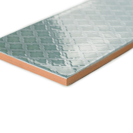 A ceramic tile displays a glossy, geometric pattern with interlocking shapes in light blue hues, set against a white background.