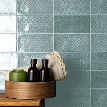 Turquoise tiles feature intricate geometric and scallop patterns. A wooden tray holds bottles and a folded cloth on a wooden sur