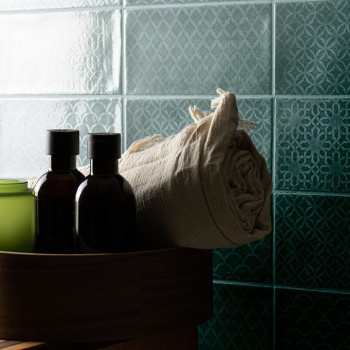 Tiled wall with intricate geometric patterns. foreground shows a round wooden container holding dark bottles and a rolled beige 