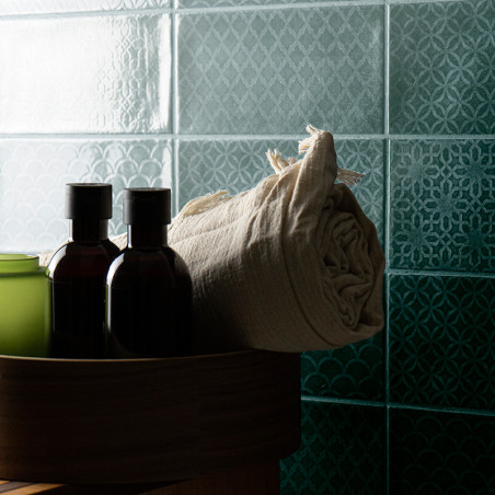 Tiled wall with intricate geometric patterns. foreground shows a round wooden container holding dark bottles and a rolled beige 