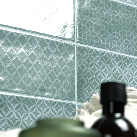 Blue-green tiles feature intricate geometric patterns, reflecting light, with blurred bottles and towels in the foreground, crea