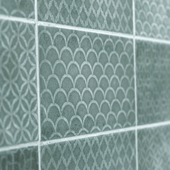 Green ceramic tiles display intricate, repeating patterns of arches and diamonds, creating a textured, decorative wall surface.