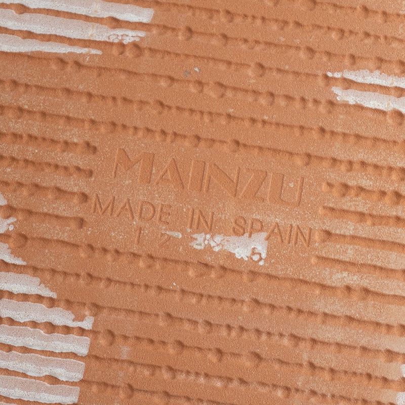 O ladrilho de terracota é gravado com `Mainzu Made in Spain`, apresentando padrões diagonais estriados e listras brancas interca
