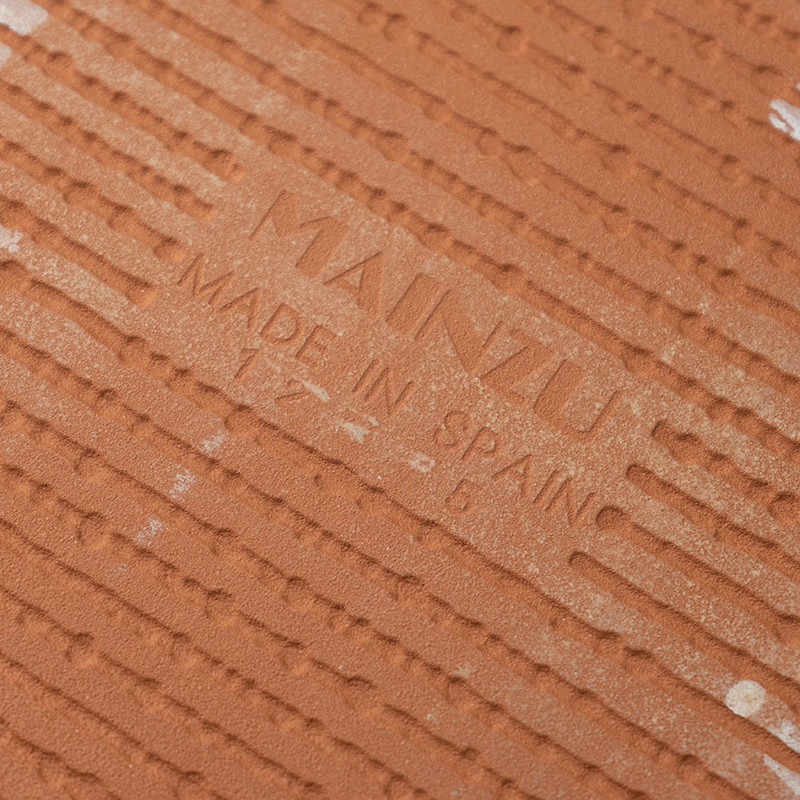 Auf der Terrakottafliese ist in der Mitte der Text „MAINZU MADE IN SPAIN“ eingeprägt, umgeben von parallelen Rillen für die Text