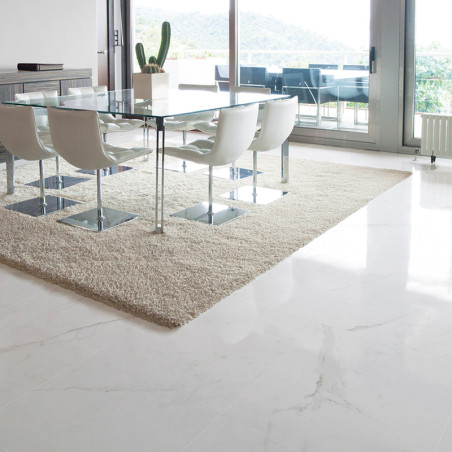 Een eethoek is voorzien van een glazen tafel met witte stoelen op een beige tapijt, omgeven door lichte marmeren vloeren en grot