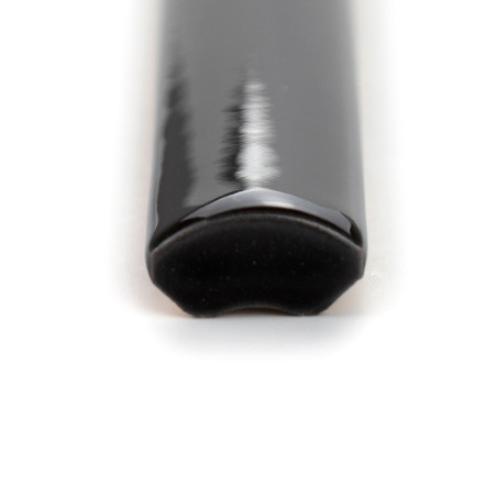 Eine glänzende, schwarze, viertelrunde Keramikfliese mit einer glatten, geschwungenen Kante ruht auf einem schlichten, weißen Hi