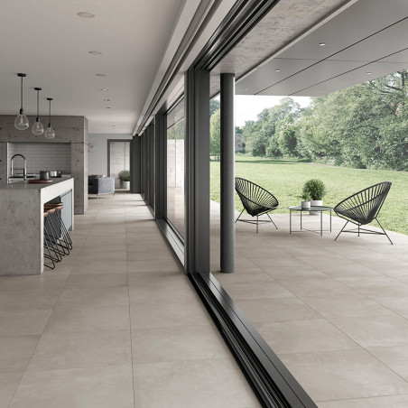 Crèmekleurige tegels strekken zich uit van een open keuken, via glazen schuifdeuren, naar een patio met moderne stoelen en weeld