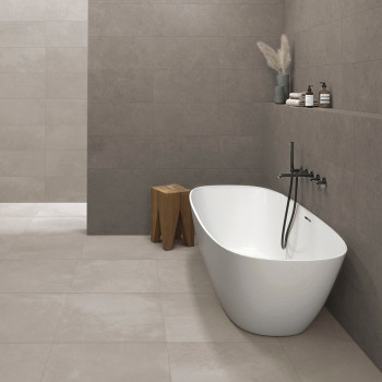 Une baignoire blanche moderne repose sur de grands carreaux beiges, à côté d’un mur au décor minimaliste comprenant un tabouret 