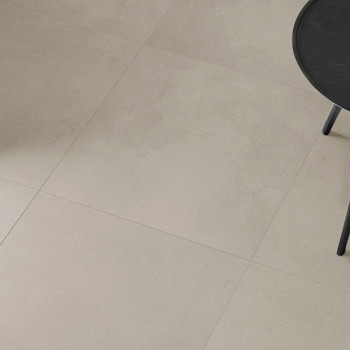 Les carreaux de céramique beige clair forment un sol lisse et propre. Une table circulaire partiellement noire avec des pieds fi