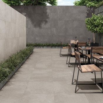 Patio extérieur avec carrelage gris. les chaises et les tables en bois sont disposées avec désinvolture. Une verdure luxuriante 