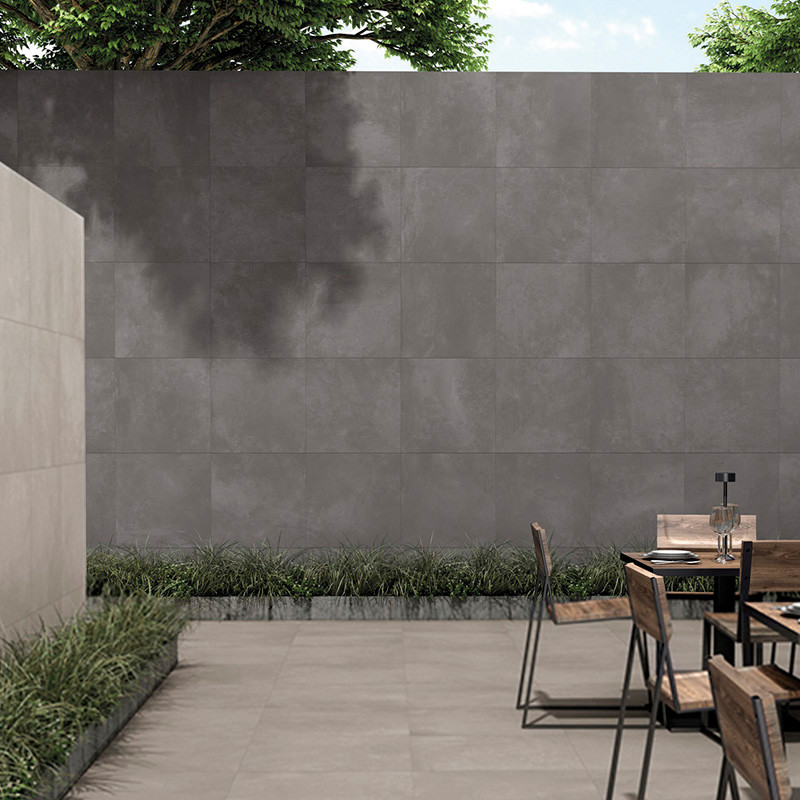 Un patio de hormigón minimalista cuenta con sillas de madera alrededor de una mesa de metal, bordeado por una pared de azulejos 