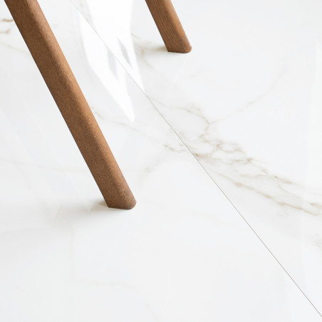 Ein Tischbein aus Holz steht auf einer glänzenden, weißen Marmorfliese mit dezenter grauer Maserung und schafft eine minimalisti Ein Tischbein aus Holz steht auf einer glänzenden, weißen Marmorfliese mit dezenter grauer Maserung und schafft eine minimalisti