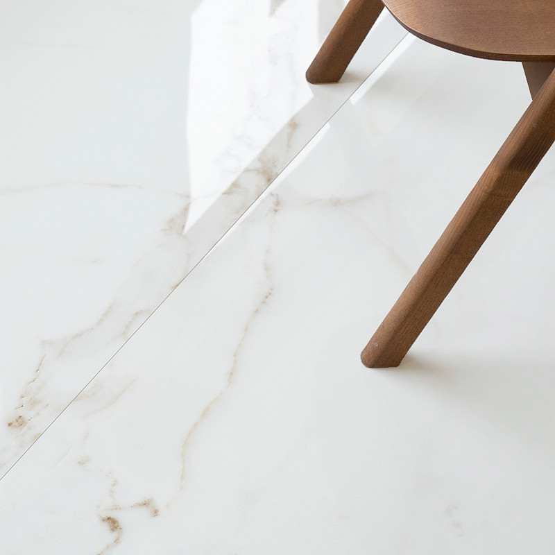 En el suelo hay un azulejo blanco brillante con sutiles vetas grises, parcialmente bordeado por la pata de una silla de madera a