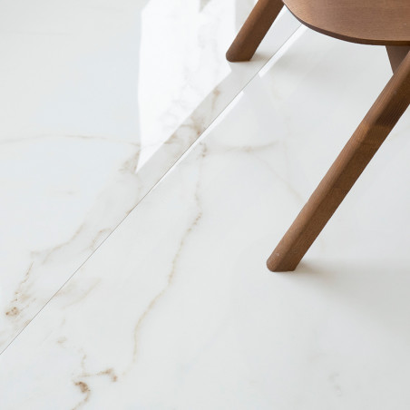 Op de vloer ligt een glanzend witte tegel met subtiele grijze nerven, rechts gedeeltelijk omzoomd door een houten stoelpoot.