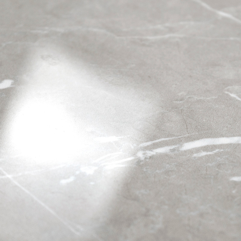 A smooth, glossy marble tile reflects a bright light. The surface features subtle gray and white veining, suggesting a polished 
