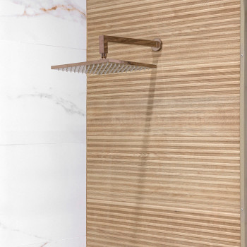 Een vierkante, metalen douchekop steekt uit een muur, afgezet tegen verticaal gestreept hout en aangrenzende witmarmeren tegels.
