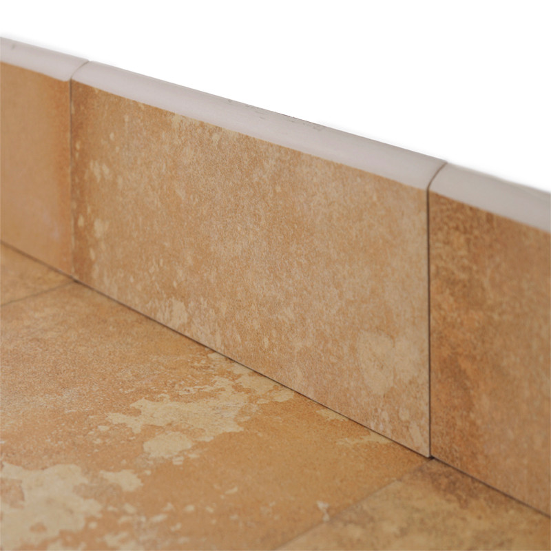 Beige keramische plinten bevinden zich aan de voet van een muur, hebben een lichte textuur, omgeven door voeglijnen en aangrenzende plinten, wat een vloerconfiguratie aangeeft.