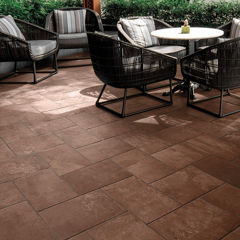 Los azulejos cuadrados marrones forman una superficie de patio. Sillas de mimbre rodean una pequeña mesa blanca, ubicada en un á