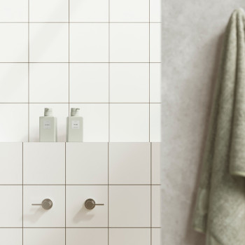 White tiles form a bathroom wall with two cylindrical handles below two bottles labeled `HAIR` and `BODY.` A green towel hangs n