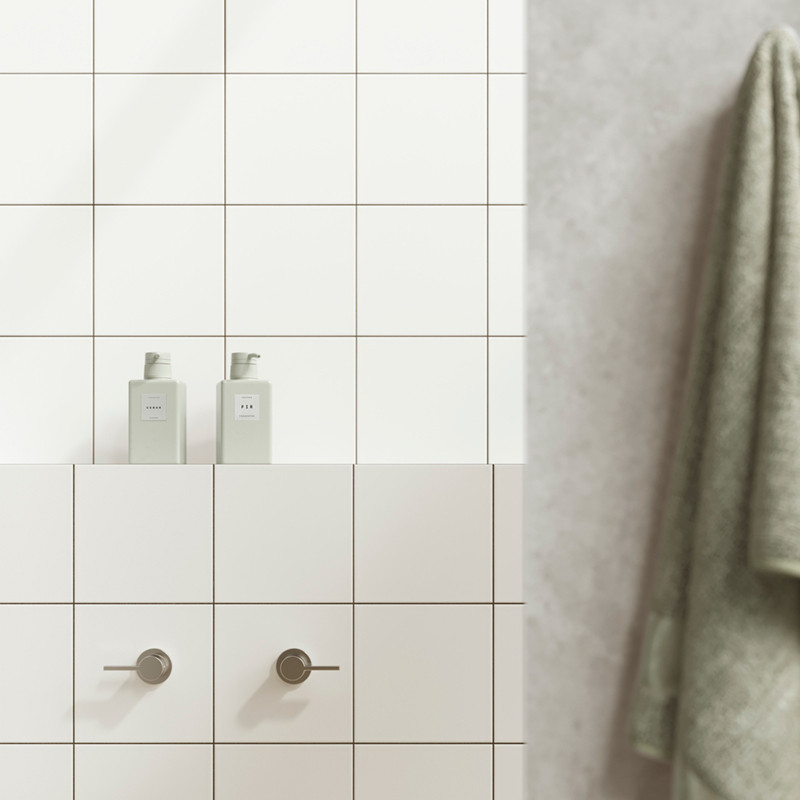 Los azulejos blancos forman una pared de baño con dos manijas cilíndricas debajo de dos botellas con las etiquetas `PELO` y `CUE
