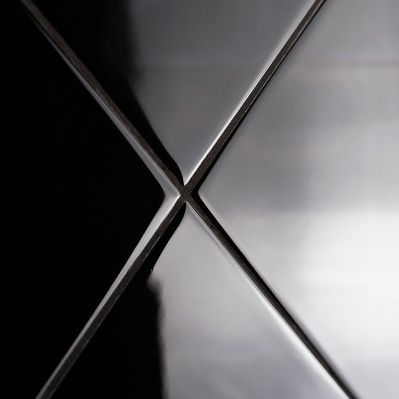 Four glossy, black ceramic tiles meet at a central point, forming an `X` with light reflections accentuating their smooth surfac