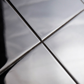 Quatro ladrilhos metálicos brilhantes estão alinhados em uma grade, refletindo luz e sombras. Eles formam linhas que se cruzam, 