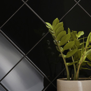 Ladrilhos pretos brilhantes formam um padrão diagonal na parede, destacando sua superfície elegante. Um vaso de planta com folha