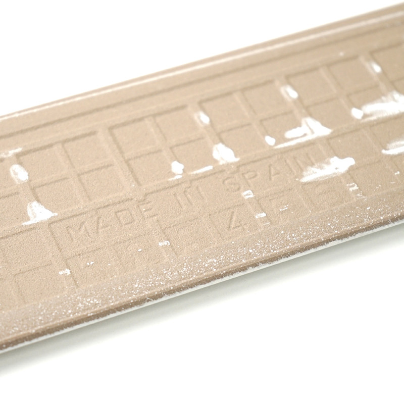 Los rodapies rectangulares de color beige texturizado muestran el texto en relieve `MADE IN SPAIN` entre tenues marcas blancas, colocados sobre un fondo blanco liso.