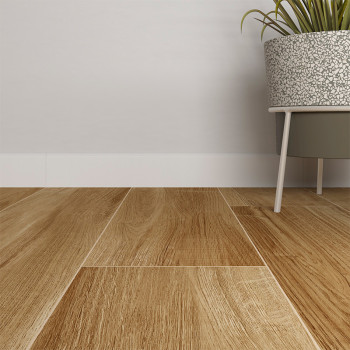 Carefully arranged wooden skirting boards, resembling natural oak boards. Next to them, a gray pot on legs holds a green plant, leaning against a plain white wall.