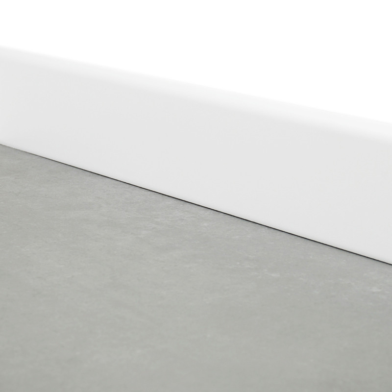 A plain gray baseboard sits flat, bordered by a white baseboard, at the intersection between floor and wall in a minimalist room.
