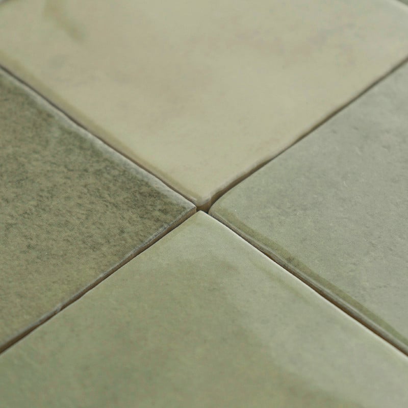 Four square, glossy ceramic tiles fit together seamlessly, colored in muted shades of green and beige, under soft lighting.