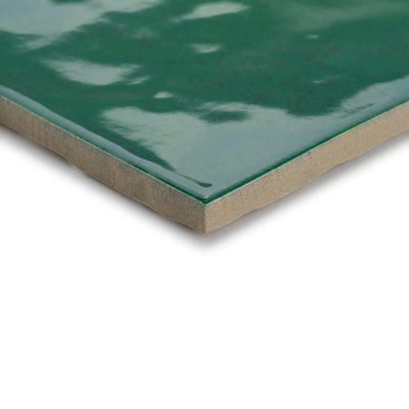 Un carreau de céramique vert brillant avec une surface polie reflète la lumière. les bords des carreaux révèlent une base beige,