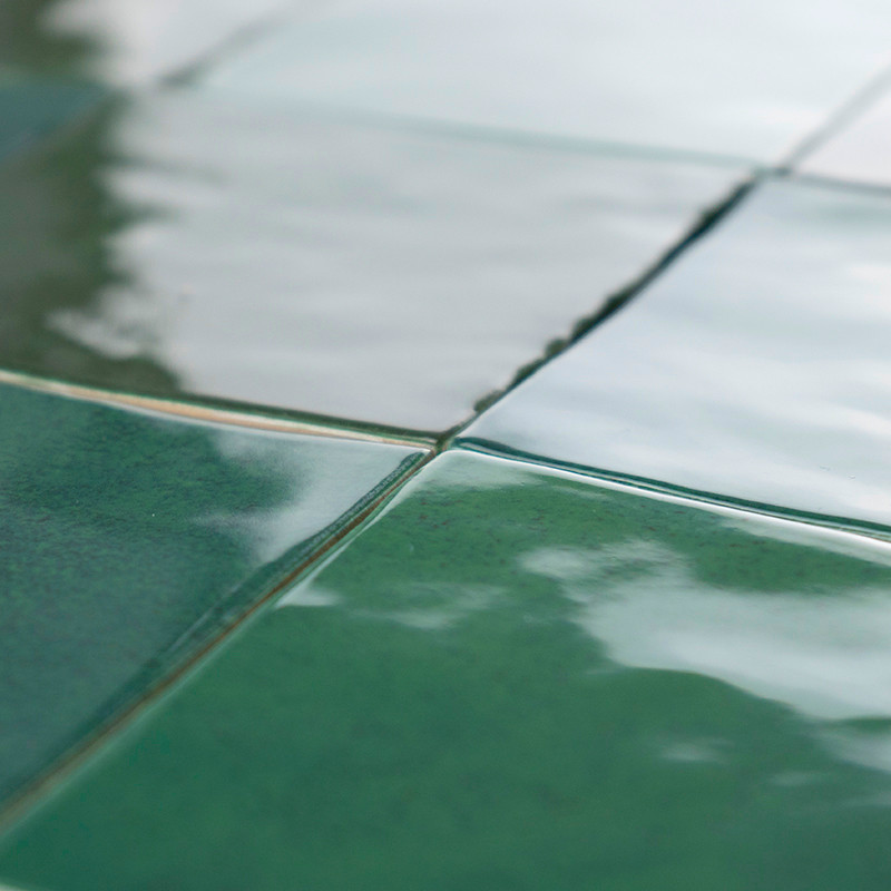 Les carreaux de céramique verte forment un motif en grille, réfléchissant la lumière avec une finition brillante, créant une sur