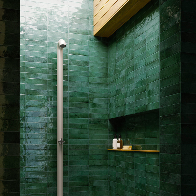 A vertical white showerhead is positioned against glossy dark green tiles in a shower. Wooden ceiling panels provide a contrasti