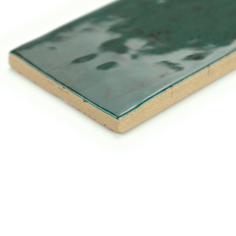 Rectangular ceramic tile with a glossy, mottled green surface, rests on a plain white background, showcasing its textured edge.
