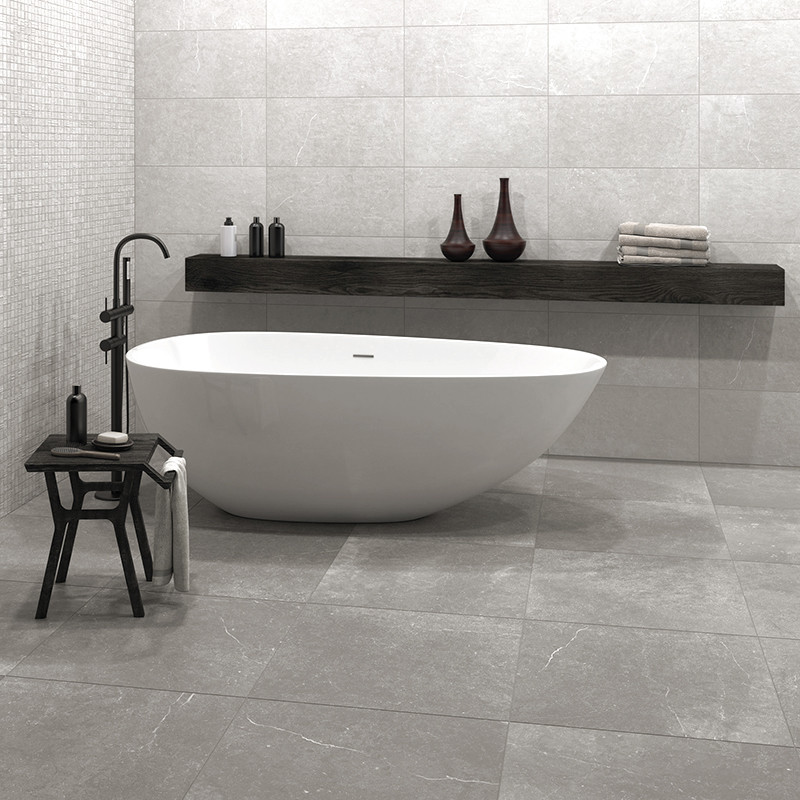 Una elegante bañera blanca se asienta sobre un suelo de azulejos grises rodeada de una decoración minimalista, que incluye un ba