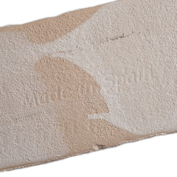 Eine rechteckige, strukturierte beige Fliese mit unregelmäßigen weißen Flecken. Der Text „Made in Spain“ ist dezent auf der Ober