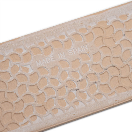 A beige ceramic tile features a repeating geometric pattern and embossed text `MADE IN SPAIN,` resting against a plain white bac A beige ceramic tile features a repeating geometric pattern and embossed text `MADE IN SPAIN,` resting against a plain white bac